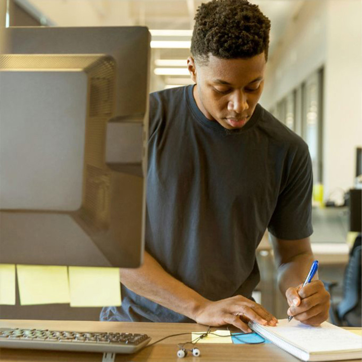 Student im modernen Büro schreibt konzentriert Notizen im Ratgeber – Alltag im praxisnahen BWL Studium.