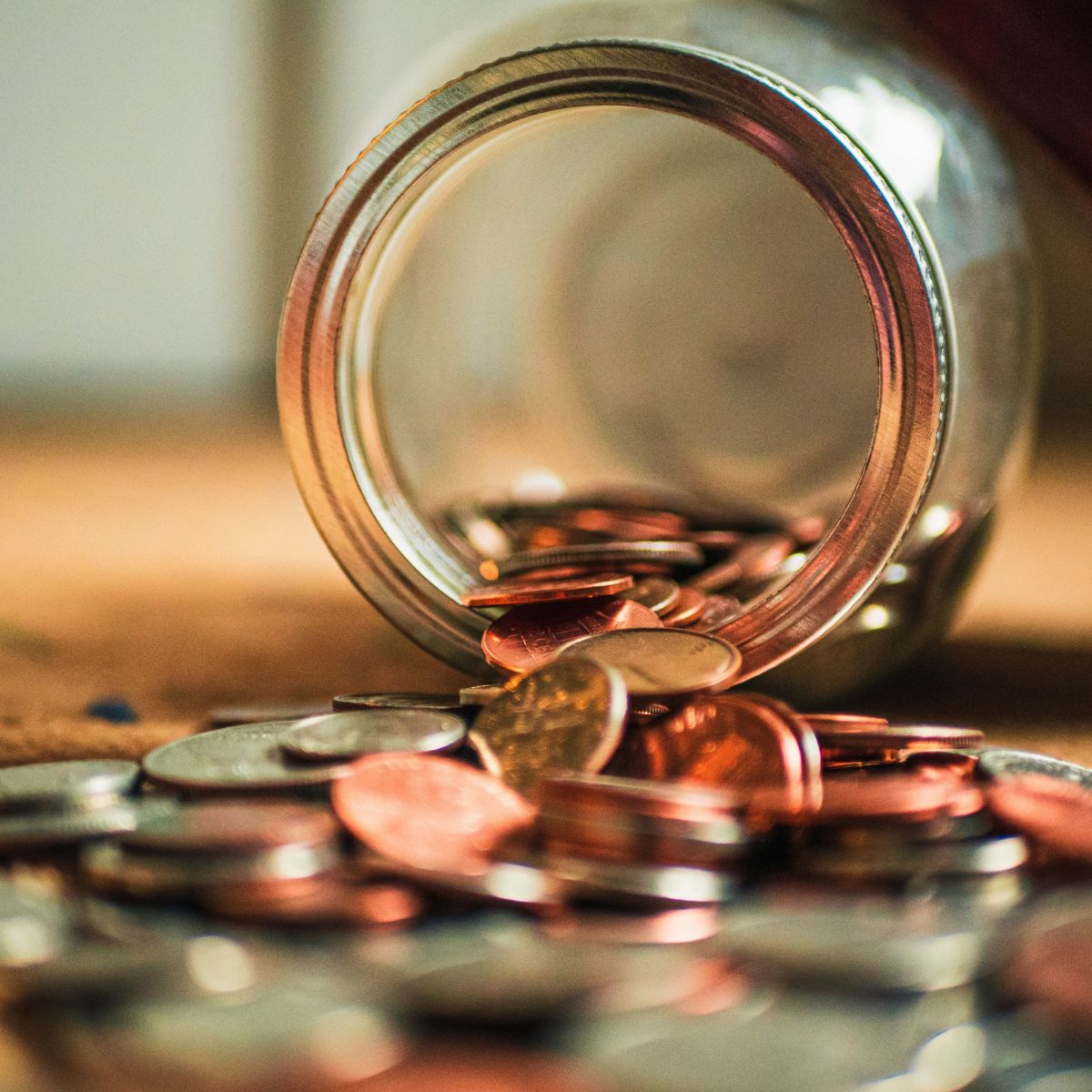 Aus einem Glas fallendes Kleingeld & sparen als Symbol für einfache Tipps zum Haushalten und Finanzplanung.