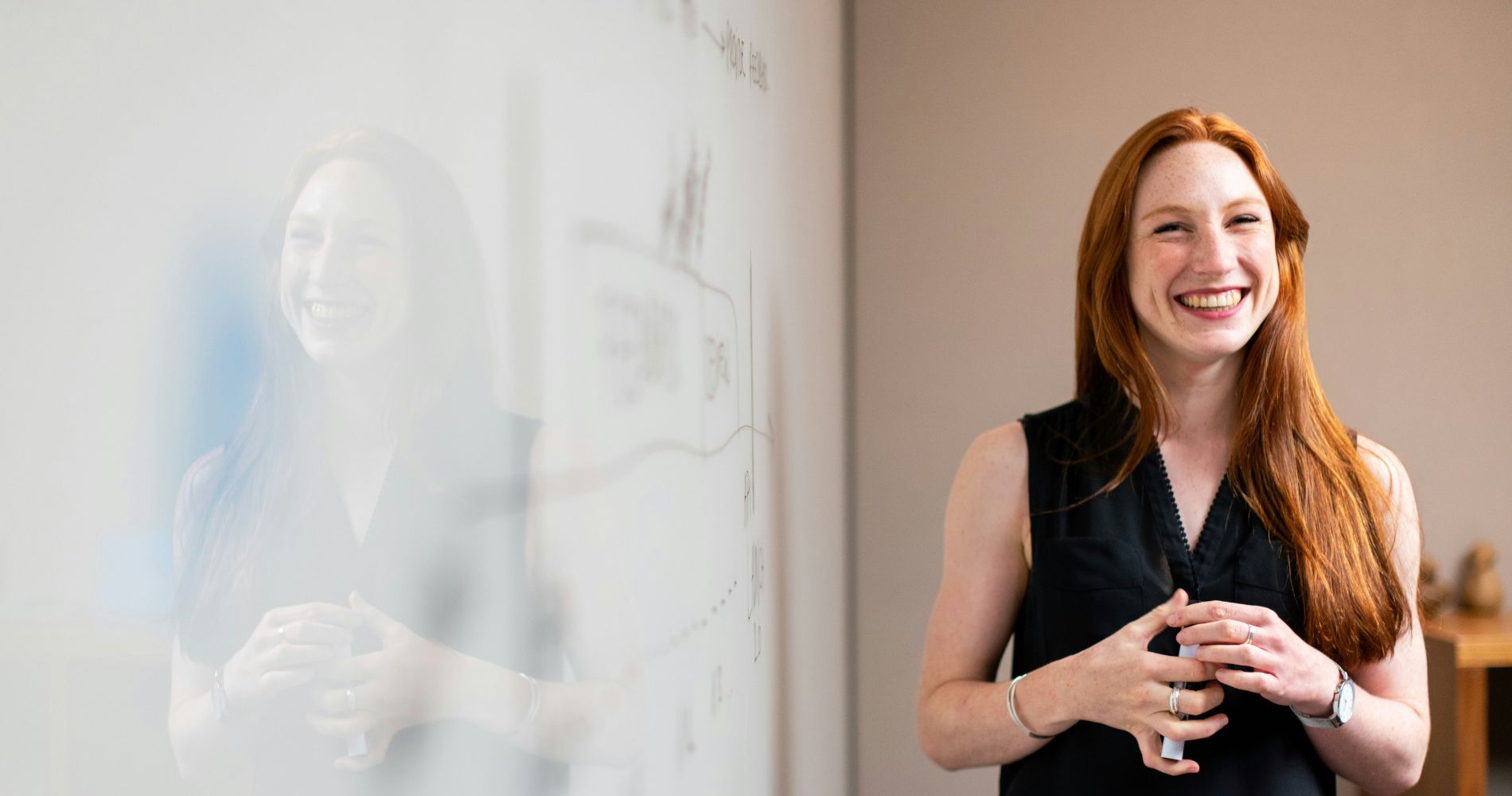 Junge Frau lächelt vor Whiteboard – sie wirkt wie ein sympathischer Ratgeber in einem Beratungsgespräch.