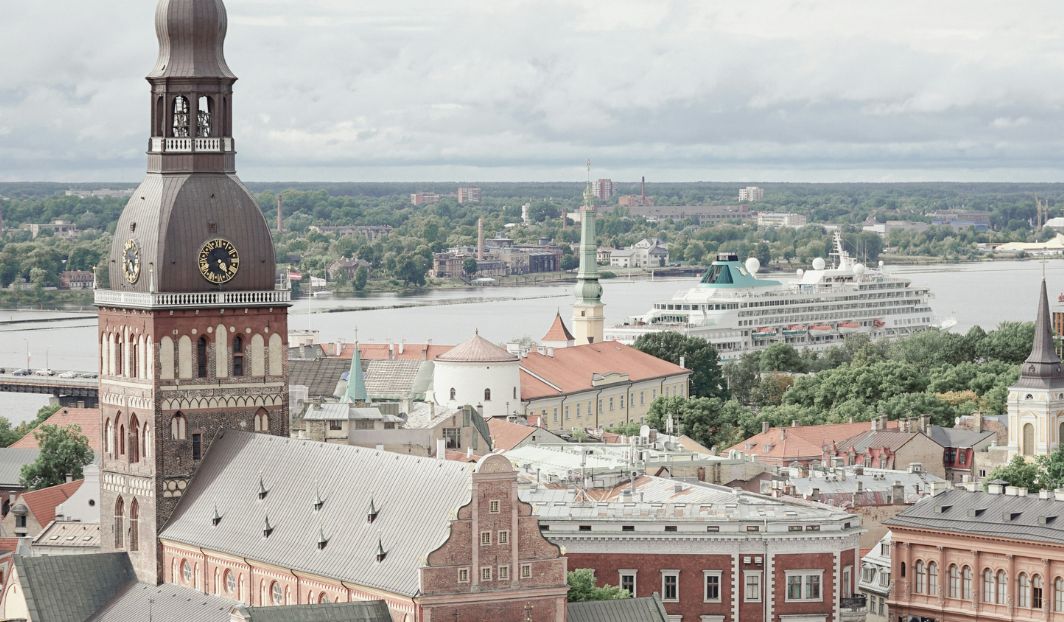 Stadtblick im Baltikum mit Kirche und Hafen, Kreuzfahrtschiff im Hintergrund, Beispiel für günstiges Reisen als Student.