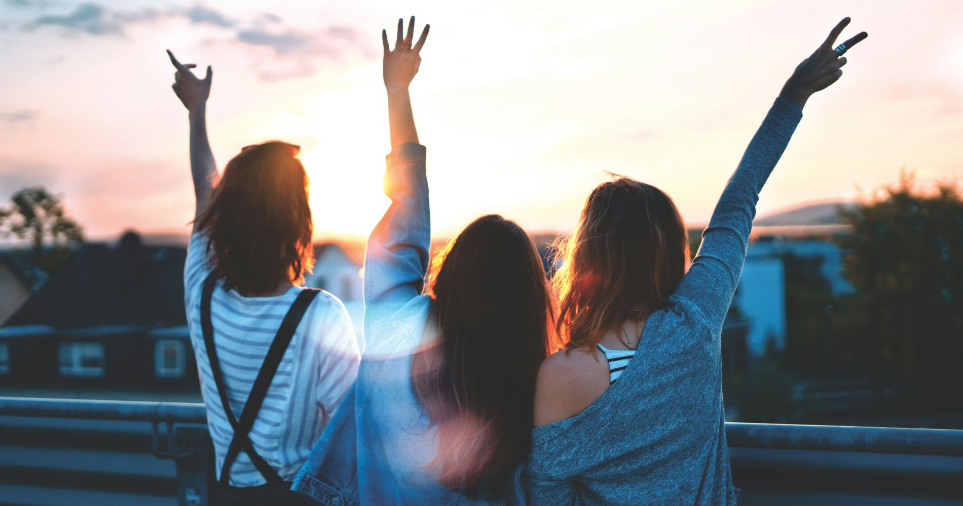 Drei junge Menschen genießen den Sonnenuntergang, heben die Arme und symbolisieren Freundschaft & eine WG Gemeinschaft.