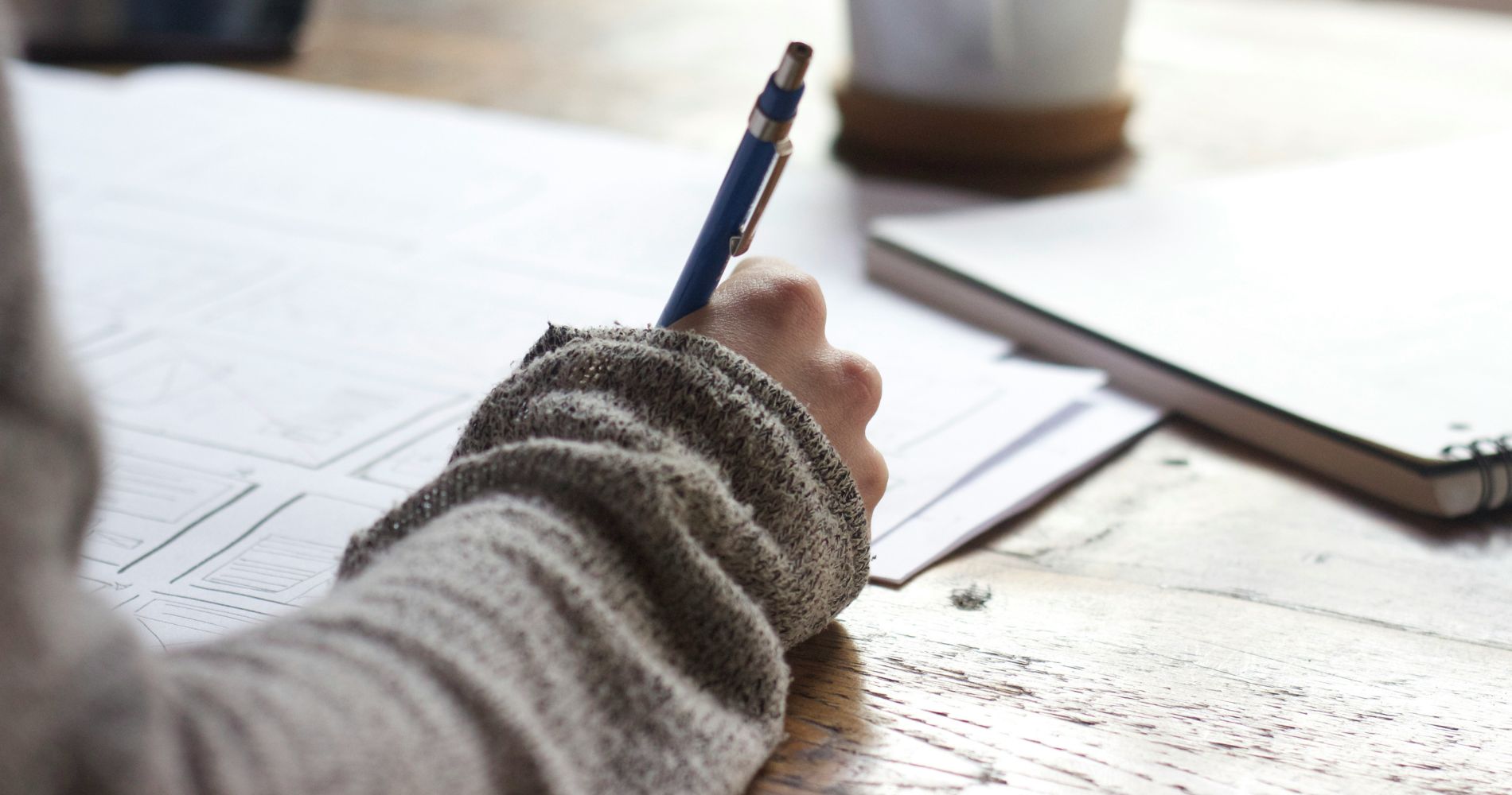 Hand mit Stift schreibt in Notizen – ein typischer Moment für konzentriertes Schreiben & Lernen am Schreibtisch.