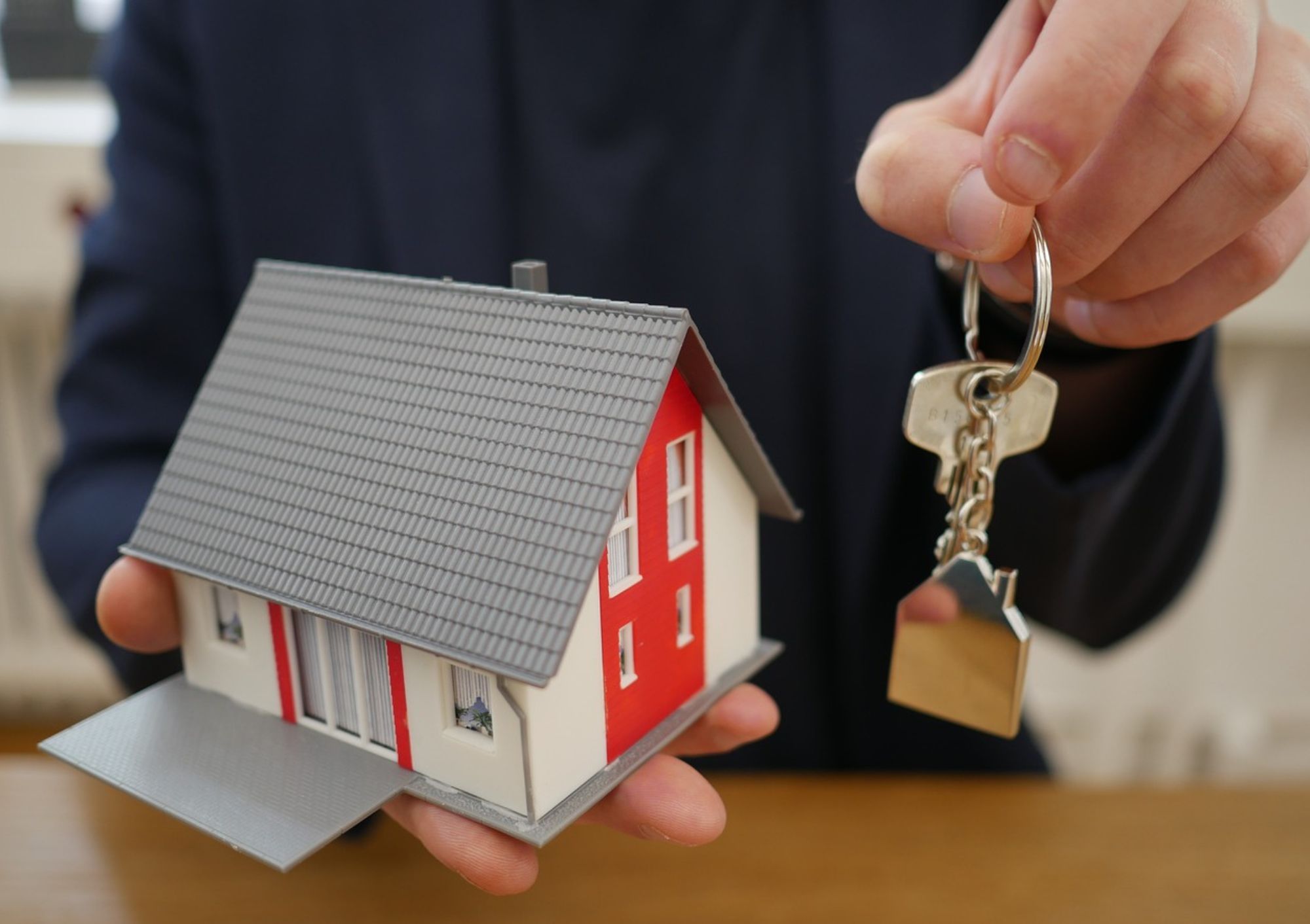 Hand hält Modellhaus und Schlüsselbund – Symbol für Praxisbezug und Karrierechancen im Immobilien Studium.