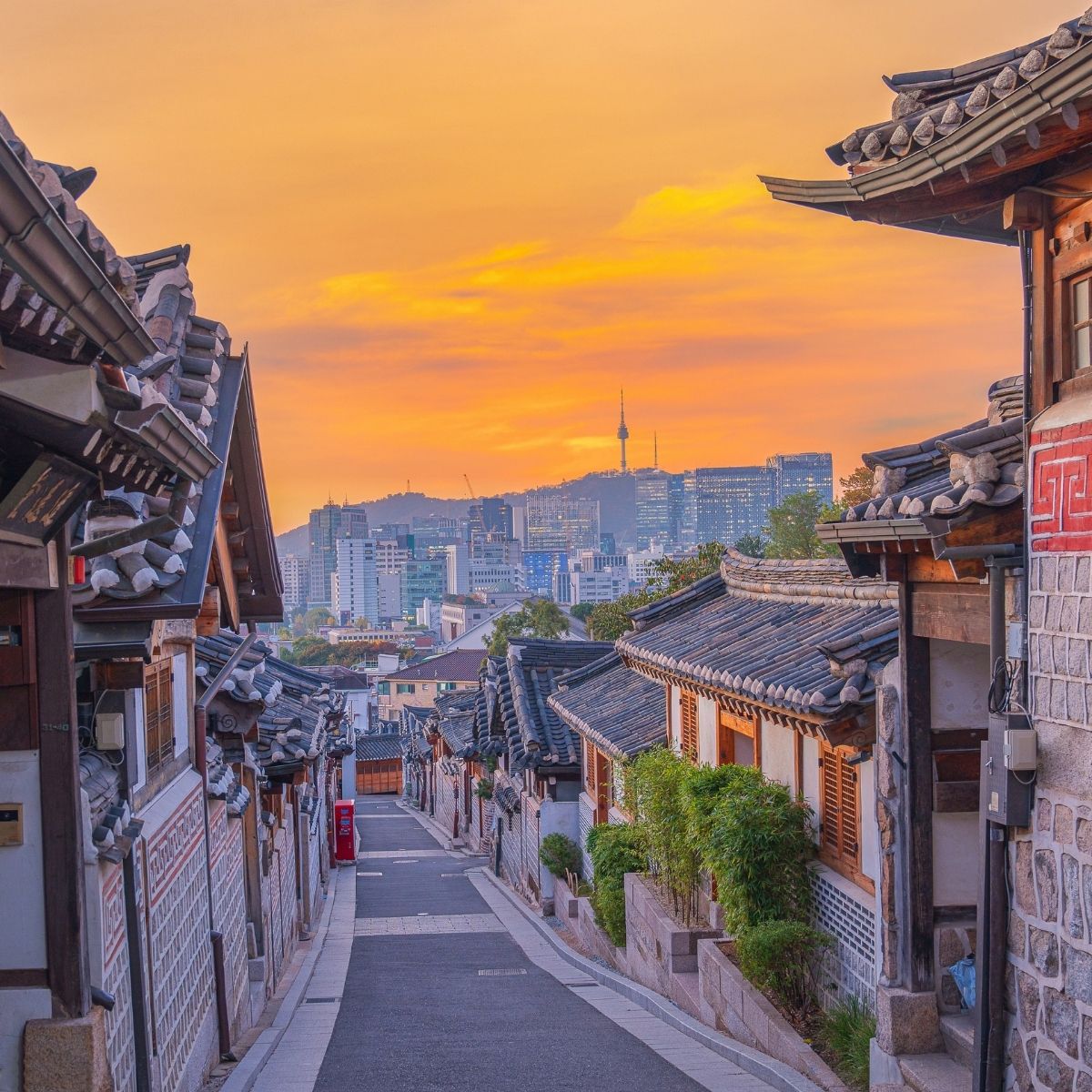 Seoul – Traditionelle Hanok-Gasse im Bukchon-Viertel bei Sonnenuntergang mit N Seoul Tower im Hintergrund.
