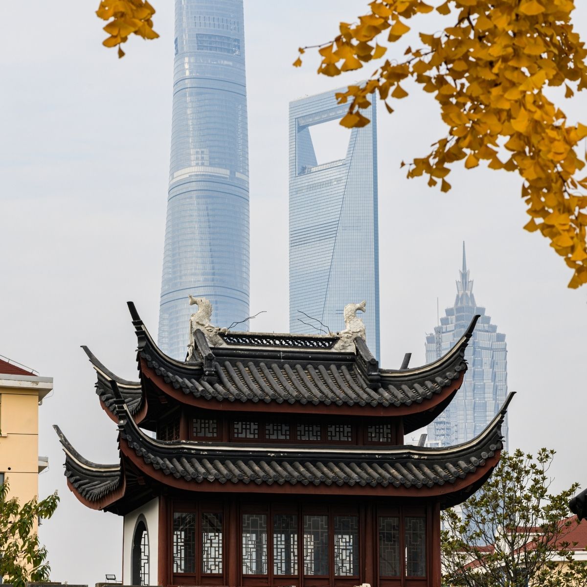 Shanghai – Klassischer Yuyuan-Pavillon mit geschwungenen Dächern vor dem Shanghai Tower im Herbstlicht.