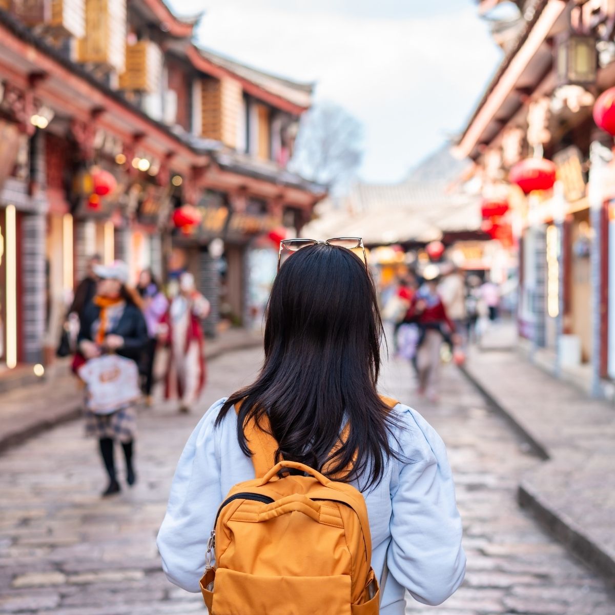 Studieren in China: Studentin mit Rucksack in traditioneller Altstadt mit chinesischen Laternen.