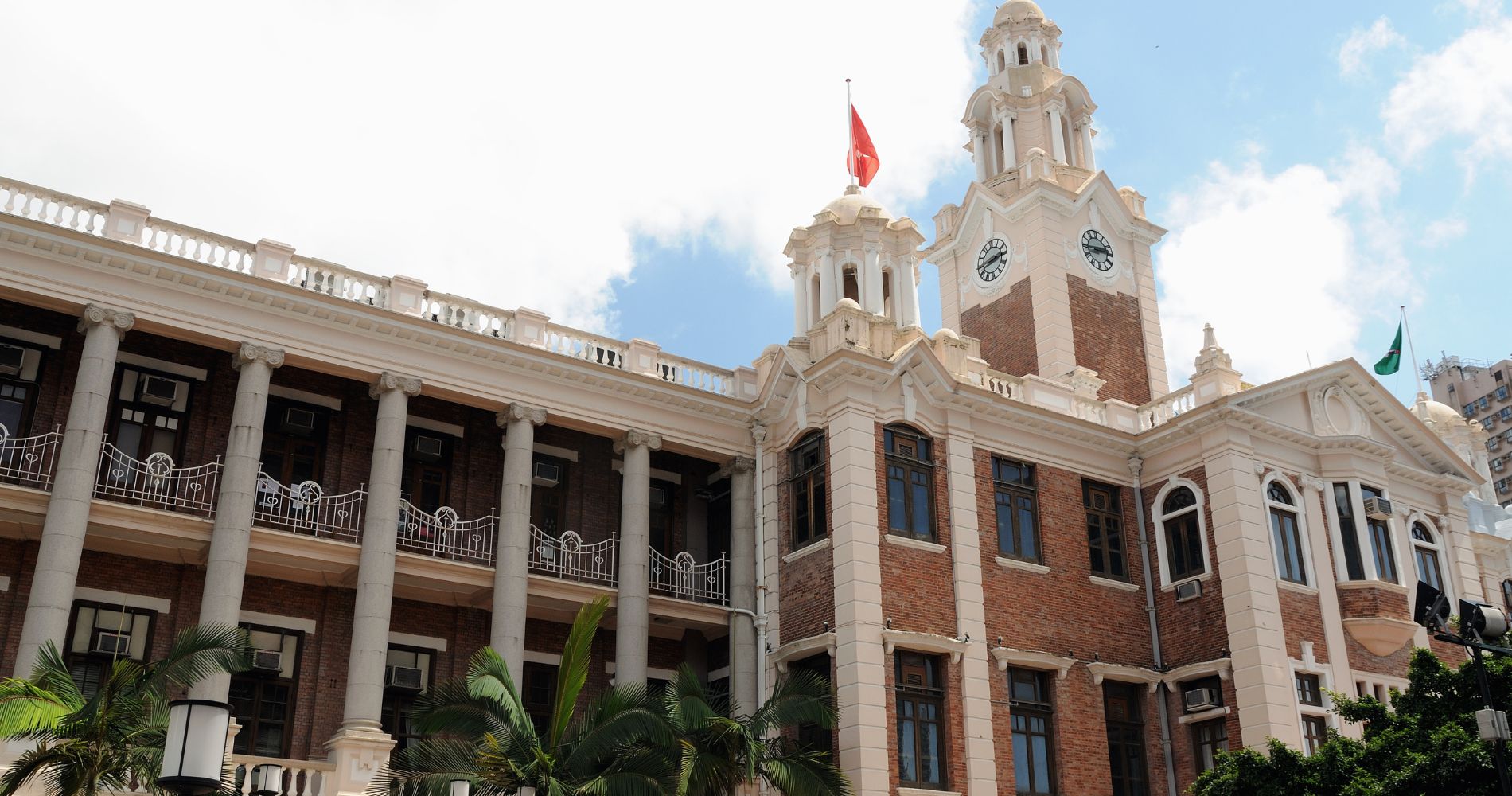 University of Hong Kong – Historisches Hauptgebäude mit Uhrturm, Backsteinarchitektur und roter Fahne im blauen Himmel.