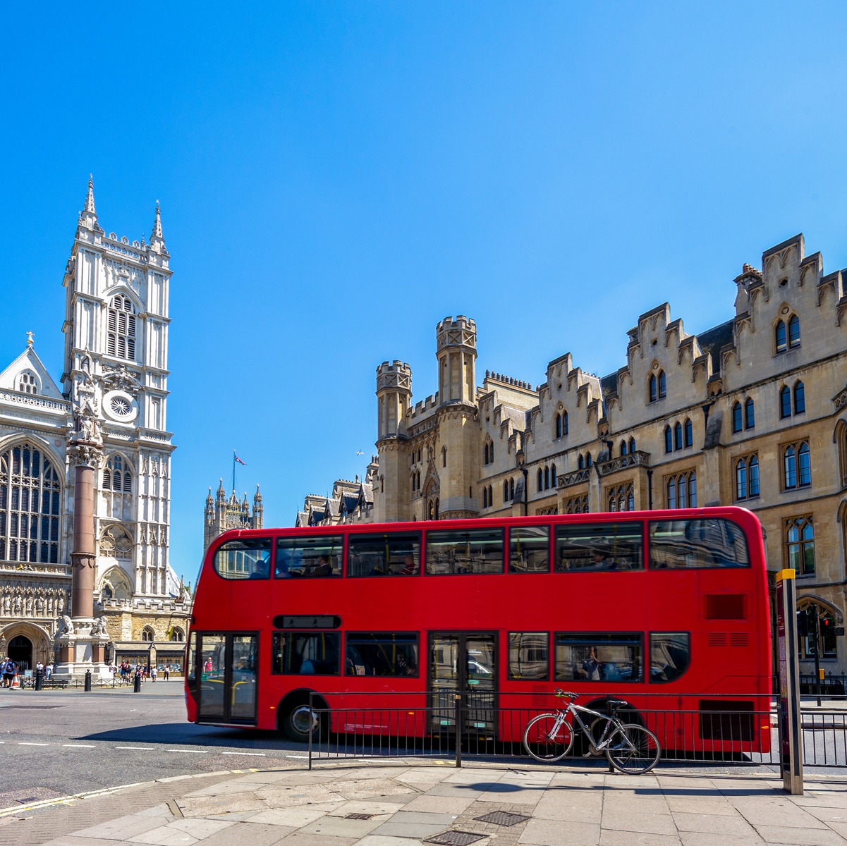 Roter Doppeldeckerbus vor der Westminster Abbey in London bei strahlendem Sonnenschein.