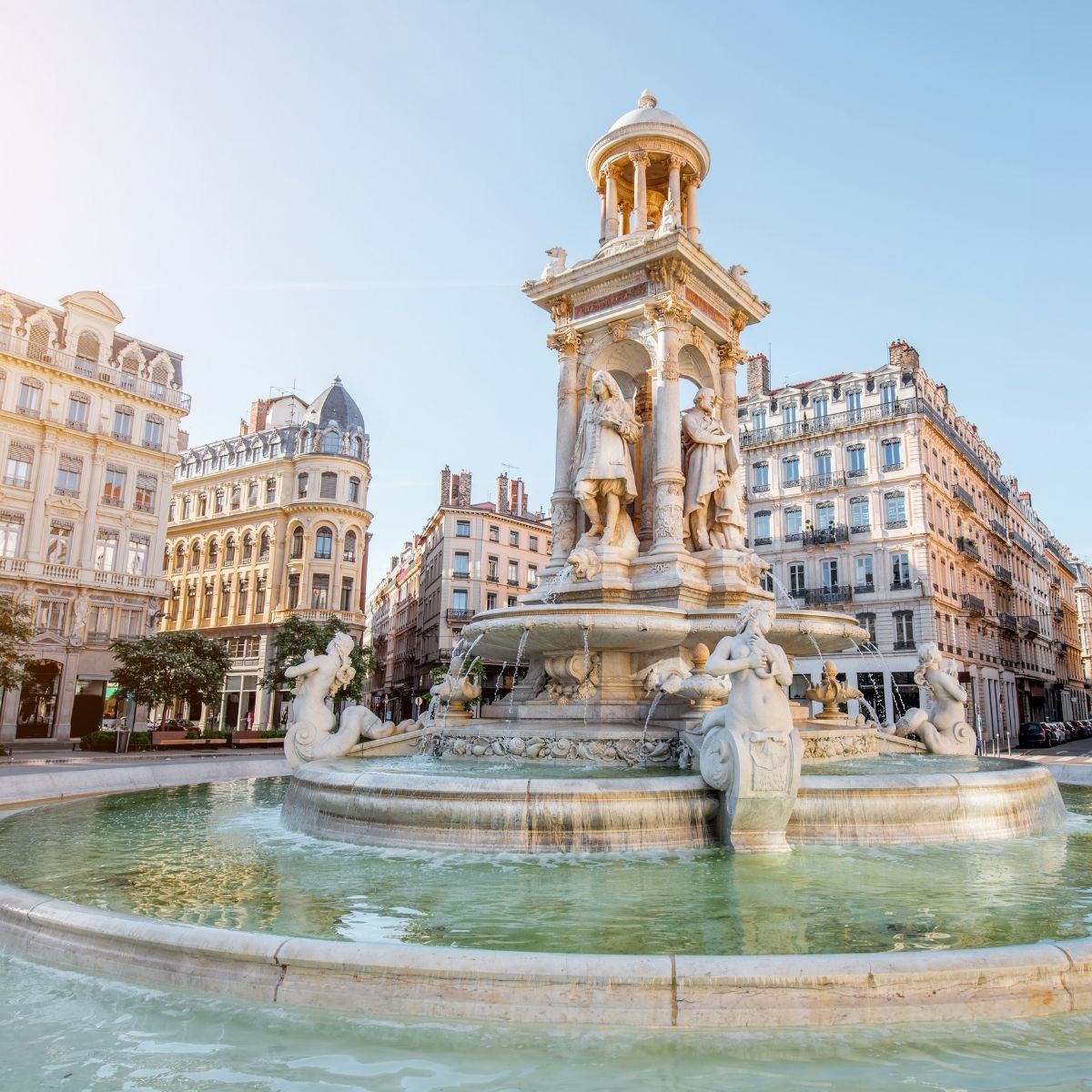 Lyon – Monumentaler Brunnen auf der Place des Jacobins mit Skulpturen und klassischer Hausfassade im Morgenlicht.