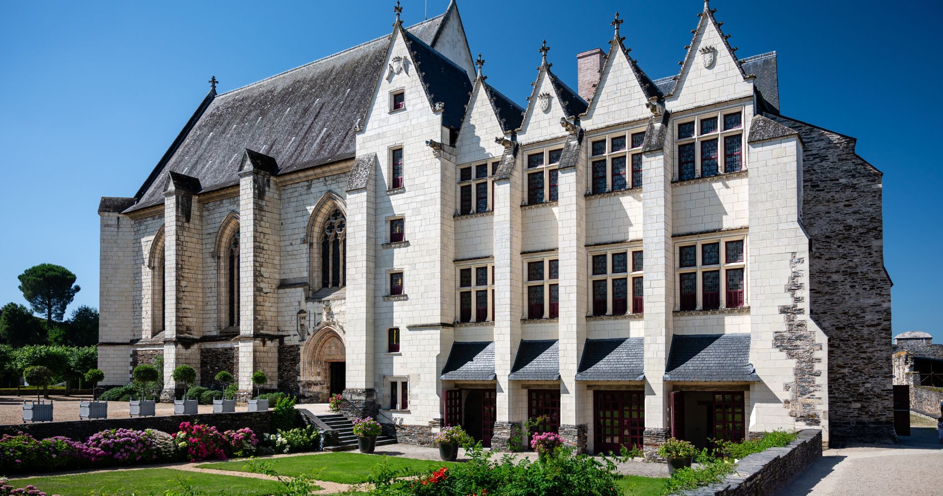 Angers – Weißes Schloss mit gotischer Kapelle, Spitzgiebeln und blühendem Garten unter strahlend blauem Himmel.