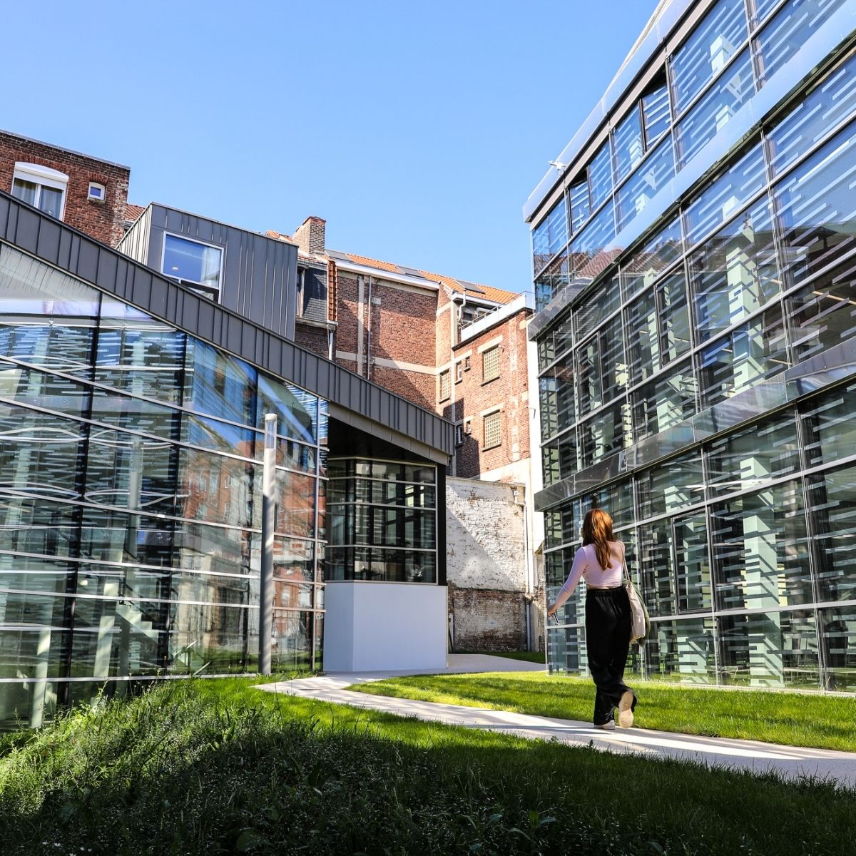 IESEG School of Management Lille – Studentin läuft zwischen modernen Glasgebäuden und historischem Backsteinbau.