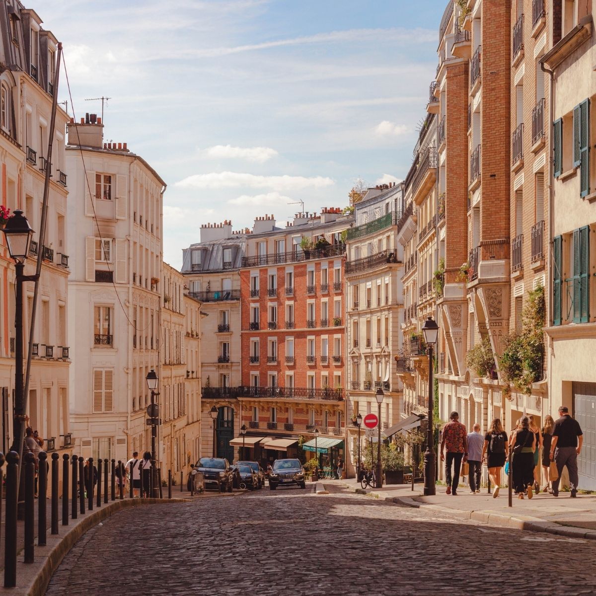 Paris – Belebte Kopfsteinpflastergasse in Montmartre mit Passanten und klassischen Hausfassaden im Sonnenlicht.