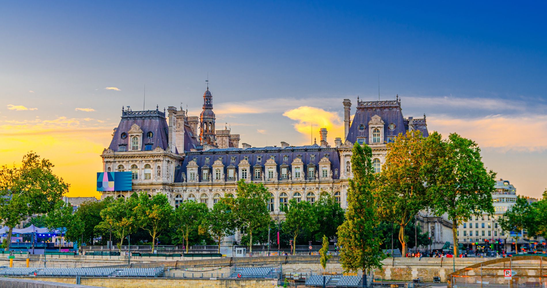Paris – Hôtel de Ville am Seineufer im Abendlicht mit prachtvoller Barockfassade und grünen Bäumen davor.