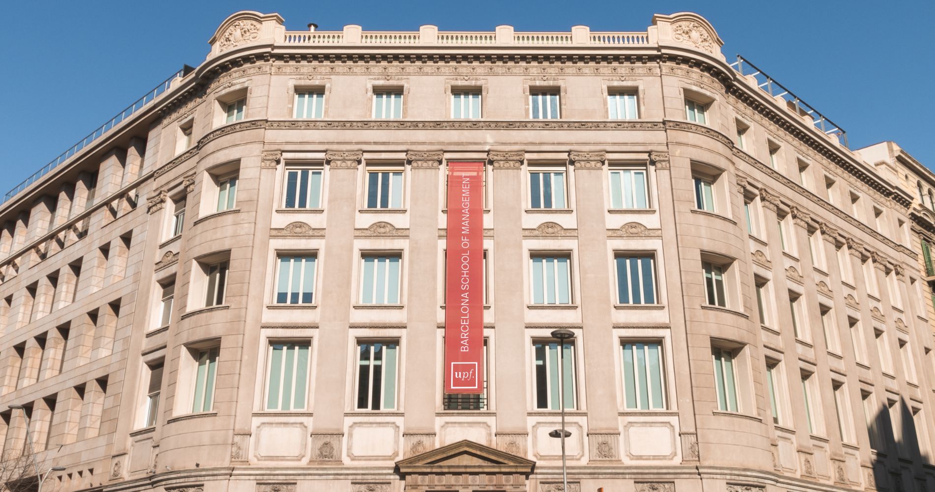 Fassade der Barcelona School of Management (UPF) mit rotem Werbebanner.