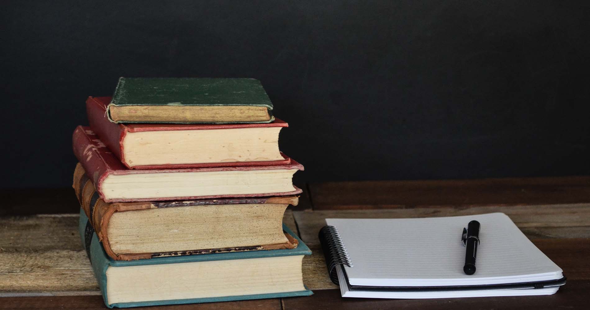 Bücherstapel aus alten Büchern mit liniertem Notizblock und Stift daneben