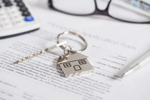 A key with a metal house as a keychain on paper documents for buying a real estate