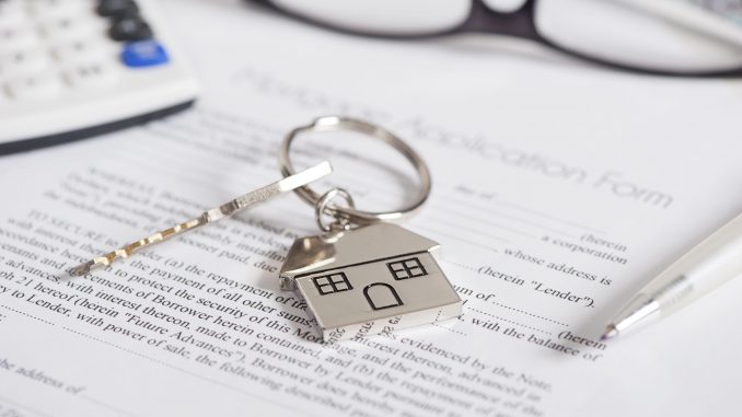 A key with a metal house as a keychain on paper documents for buying a real estate