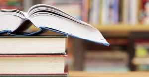 A stack of books on a table with a wall of books in the background