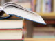 A stack of books on a table with a wall of books in the background