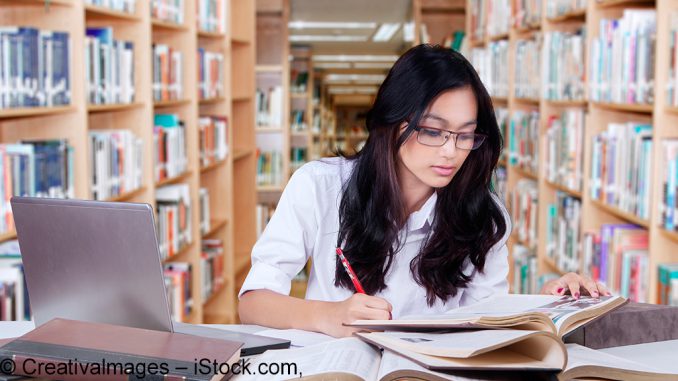 Young student writing a academic paper in the library