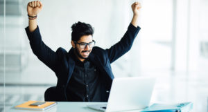 Young man cheering in front of laptop, happy about his success in email negotiations.