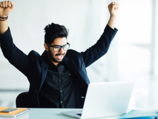 Young man cheering in front of laptop, happy about his success in email negotiations.