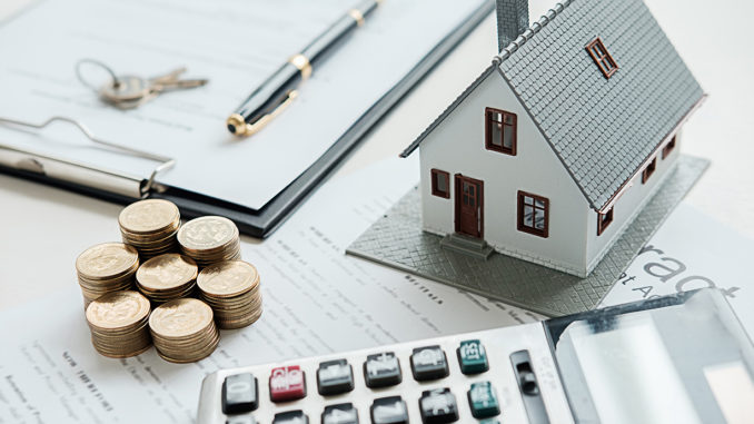 A hodgepodge of a calculator, model house, keys, documents and towers of small change on a table