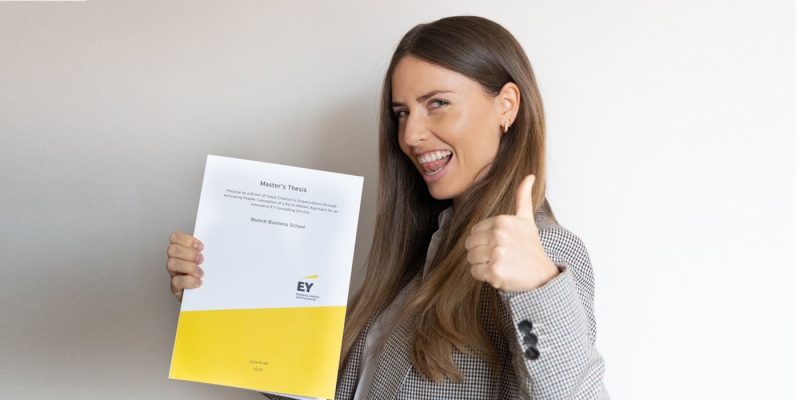 Julia Kraft, alumna of Munich Business School, with her master's thesis in hand and doing a thumbs up