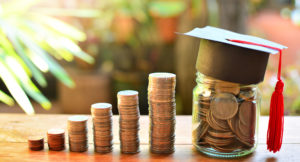 various piles of coins getting higher from left to right and a jar full of coins with a graduate hat on it