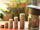 various piles of coins getting higher from left to right and a jar full of coins with a graduate hat on it