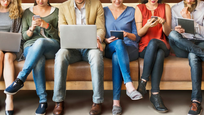 People side by side on a bench using different digital devices such as a laptop, smartphone or tablet.