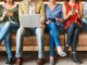 People side by side on a bench using different digital devices such as a laptop, smartphone or tablet.