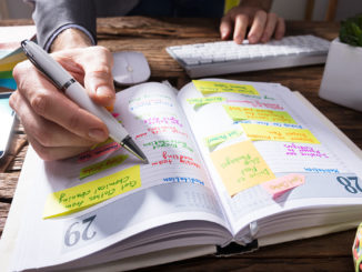 Lifelong Learning: Close-up Of A Businessperson's Hand Writing Schedule In Diary With Pen On Wooden Desk