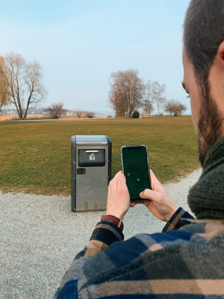 Pascal Ritter, alumnus of Munich Business School, in front of a trash can using the app "The Fortunate Planet"