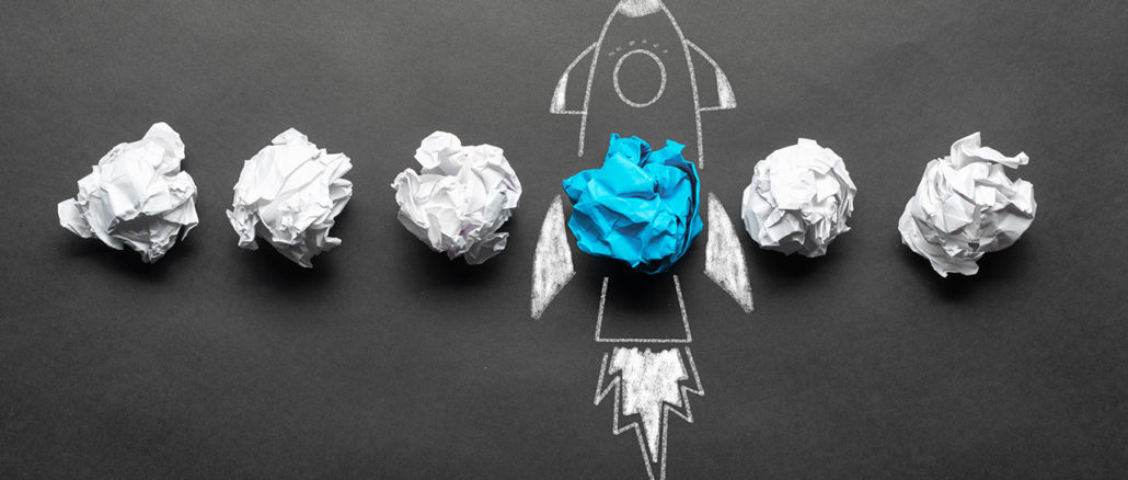 Crumpled paper balls and a rocket drawing on a blackboard.