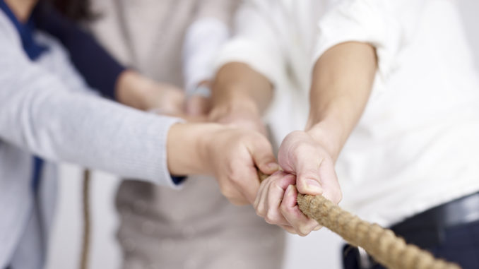 group of businesspeople playing tug-of-war, focus on hands.
