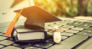 Graduate hat, scroll and book in miniature on laptop keyboard