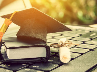 Graduate hat, scroll and book in miniature on laptop keyboard