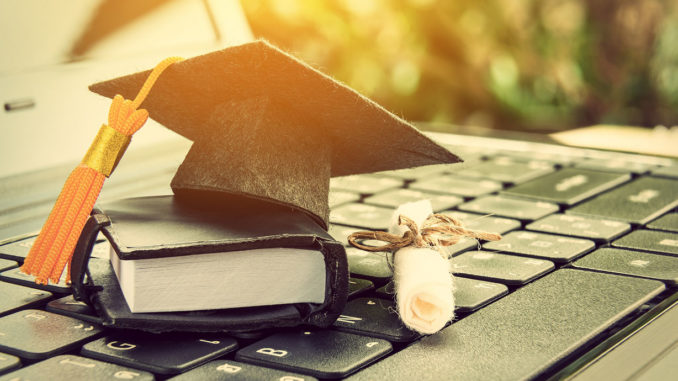 Graduate hat, scroll and book in miniature on laptop keyboard