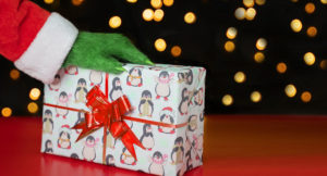 A green hairy hand in a Santa costume on a gift box against the background of Christmas lights