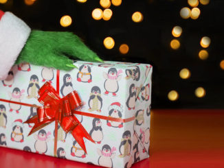 A green hairy hand in a Santa costume on a gift box against the background of Christmas lights