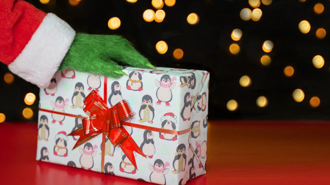 A green hairy hand in a Santa costume on a gift box against the background of Christmas lights