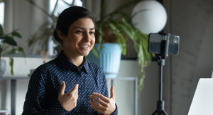 Smiling Indian young woman recording herself with her smartphone and a tripod