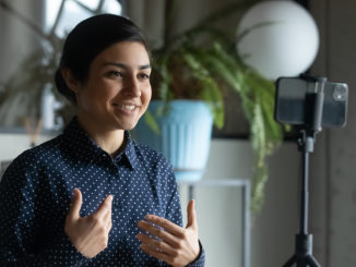 Smiling Indian young woman recording herself with her smartphone and a tripod