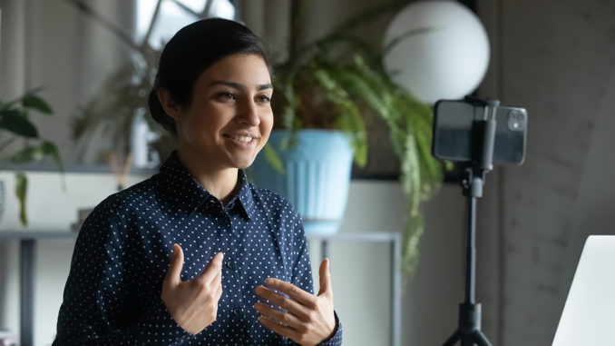 Smiling Indian young woman recording herself with her smartphone and a tripod