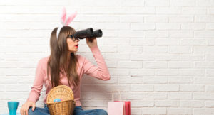 Woman with bunny ears for Easter holidays sitting on the floor and looking for something in the distance with binoculars