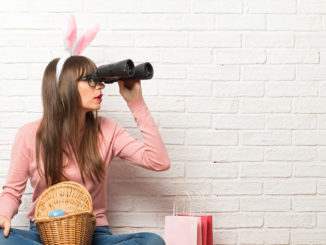 Woman with bunny ears for Easter holidays sitting on the floor and looking for something in the distance with binoculars
