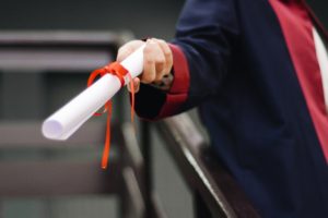 Close-up of a hand handing over a diploma as a roll of paper.