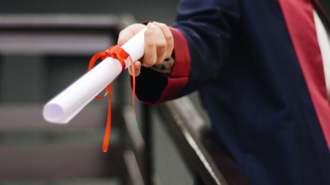 Close-up of a hand handing over a diploma as a roll of paper.