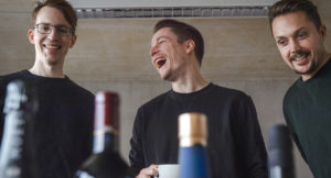 The three founders of spiritory laughing - Janis Wilczura, alumnus of Munich Business School in the middle; bottle tops in foreground